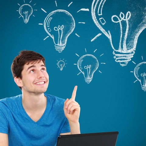 A Guy in a Blue T-shirt Smiling Is Looking Up and Pointing Up to Lightbulbs