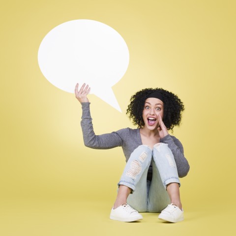 A Woman Sitting on the Ground Holding a Speech Bubble by Her Face