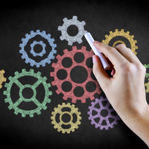 Someone Drawing Mechanical Gears on a Blackboard