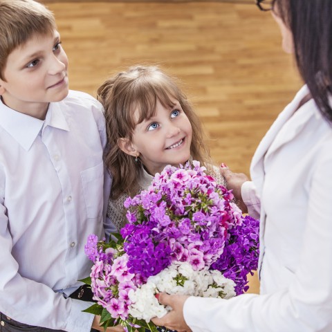 Two Young School Children Give Their Teacher a Bunch of Flowers.