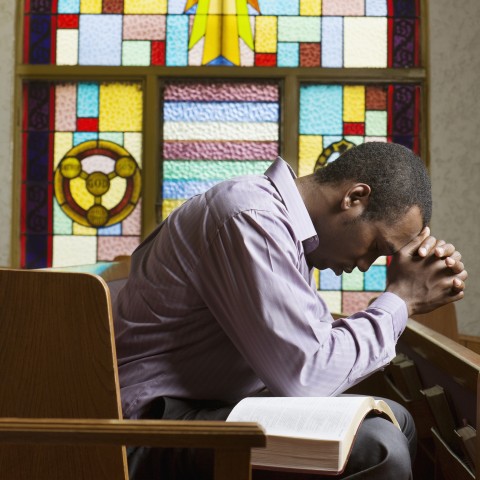 Young Man with Bible on His Lap Praying in Church