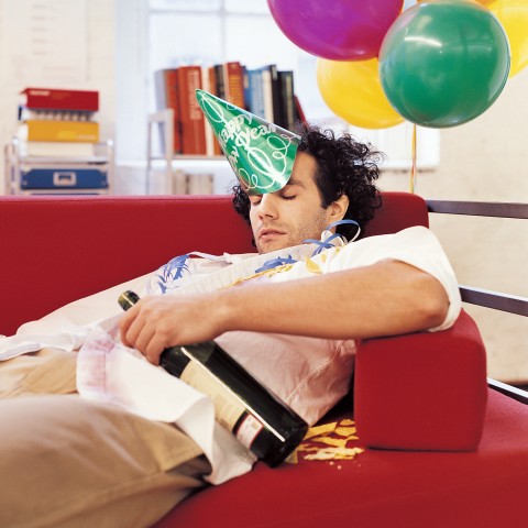 A Man Holding a Bottle while Lying Hungover on the Couch after a Party