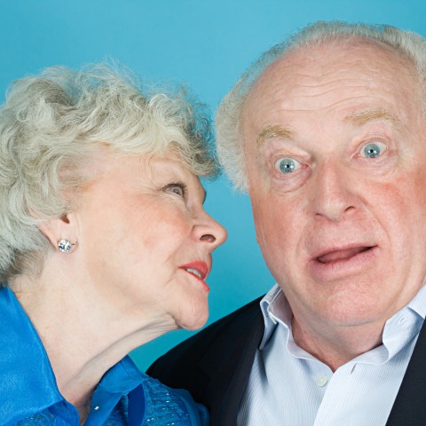 An Old Lady Whispering Something into Her Surprised Husband’s Ear