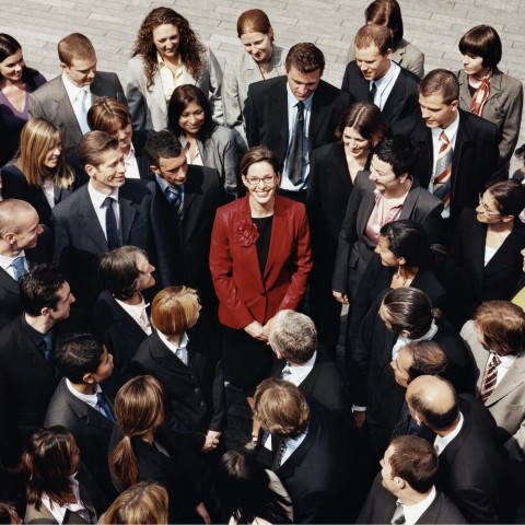 A Woman in a Red Jacket Standing in the Center of Several People in Black Suits