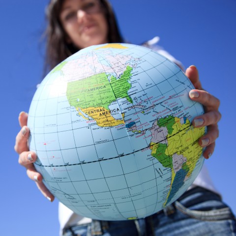 A Smiling Woman Holds a Globe in Front of Her.