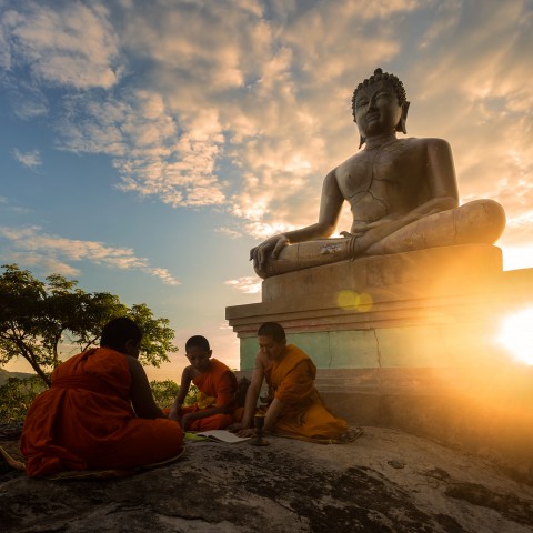 Monks reading on a boulder in front of a Buddha statue