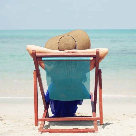 A Woman Wearing a Large Hat, Sitting in a Beach Chair by the Seaside.