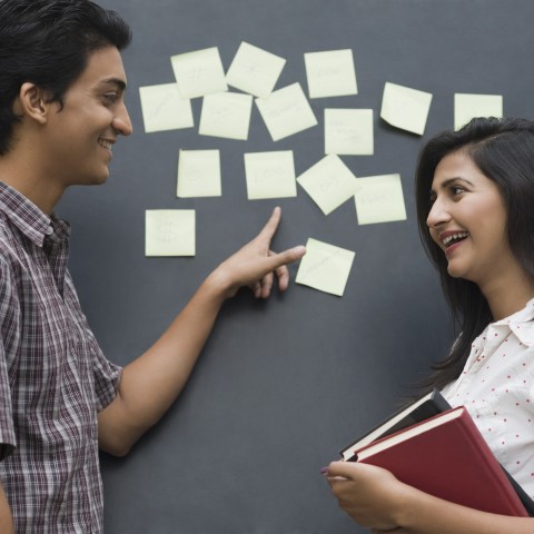 Man and Woman Talking Next to Blackboard with Sticky Notes