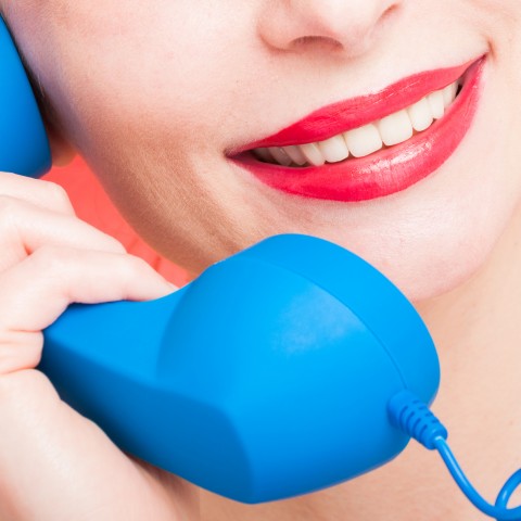 A Woman with Red Lipstick Holding the Speaker Piece of a Blue Telephone.