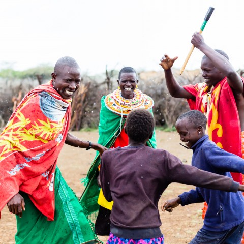 Dancers from the Kenyan Maasai Mara tribe in traditional gear playing with children.