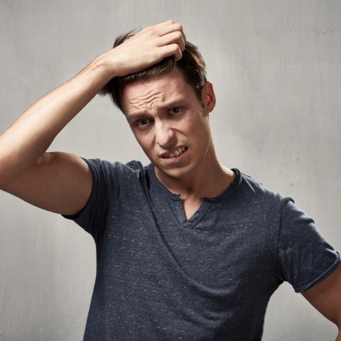 A Young Guy in a Grayish T-shirt Frowning and Scratching His Head