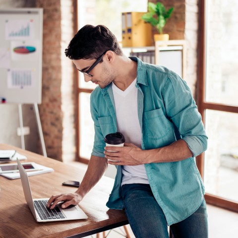 A Man Drinking Coffee and Working on His Laptop