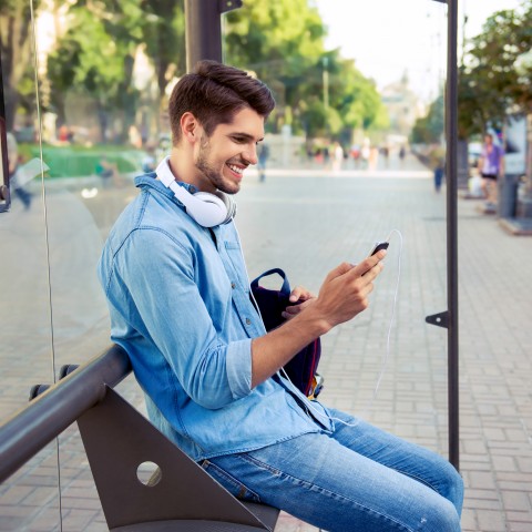A Man Sitting at a Bus Stop Using His Cellphone