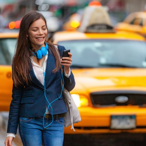 A Smiling Young Latina in a City Setting, Looking at Her Cell Phone.