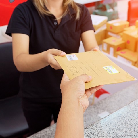 Customer handing an envelope to a clerk at a post office counter