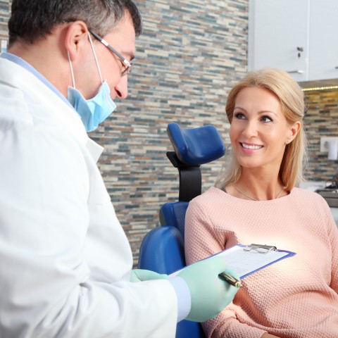 A Doctor Explaining Something to His Patient, Who Is a Blond Woman That Is Smiling and Sitting in a Chair