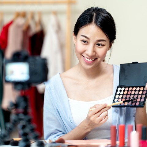 An Asian Woman Is Giving a Make-up Tutorial while Recording Herself with Her Camera, She Is Holding a Palette