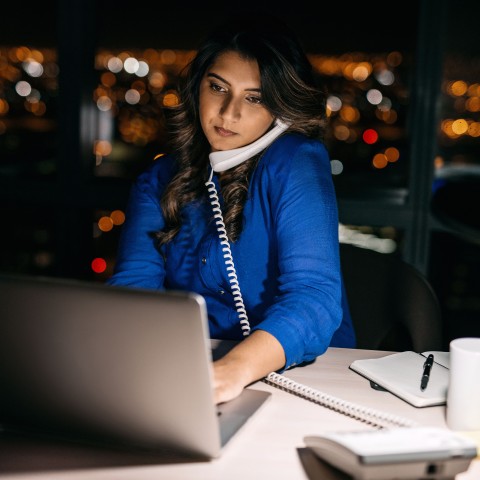 A Woman Sitting at Her Work Desk Late at Night Talking on the Phone