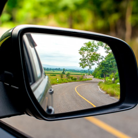 A Close-up of a Car’s Rear View Mirror Showing Nature and a Road