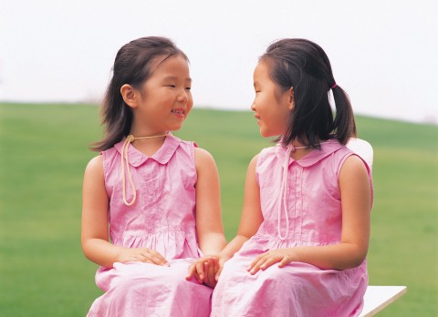 Cute Twin Girls Sitting Together on a Bench
