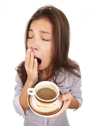 A woman yawning and holding a cup of coffee