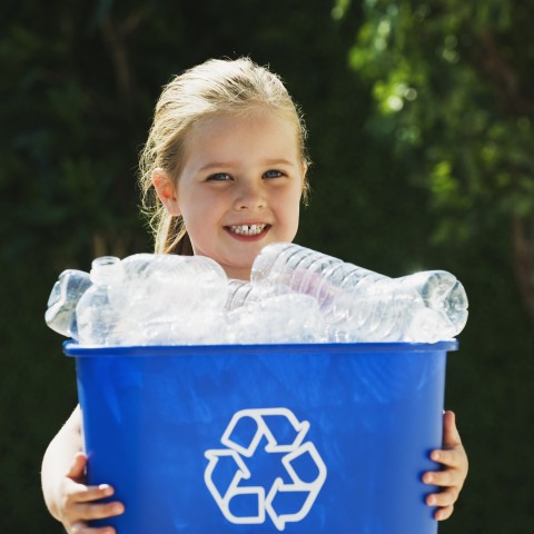 Child holding a blue recycling bin filled with plastic bottles
