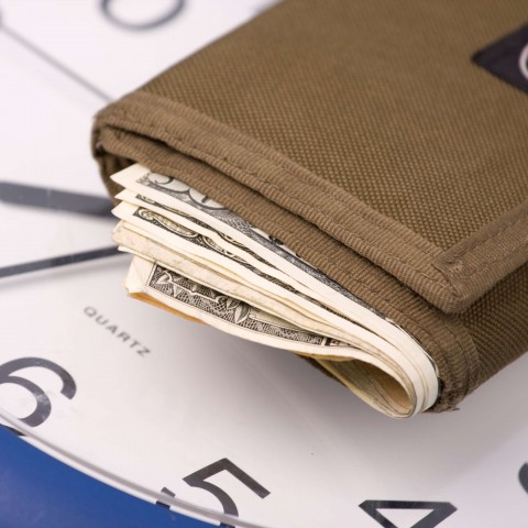 A Wallet Having Some Currency In It Placed on a Clock