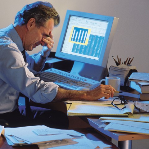 A Man Sitting at His Work Desk, Rubbing His Eyes with Exhaustion