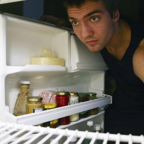 A Guy Looking into a Mostly Empty Fridge at Night