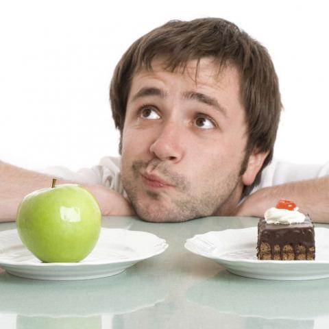 Мужчина, пытающийся выбрать между зеленым яблоком и кусочком торта