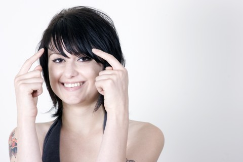 A Smiling Woman Touches Her Head with Her Index Fingers