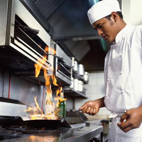 A Cook or Chef Preparing a Flambé Dish on a Restaurant Stove.